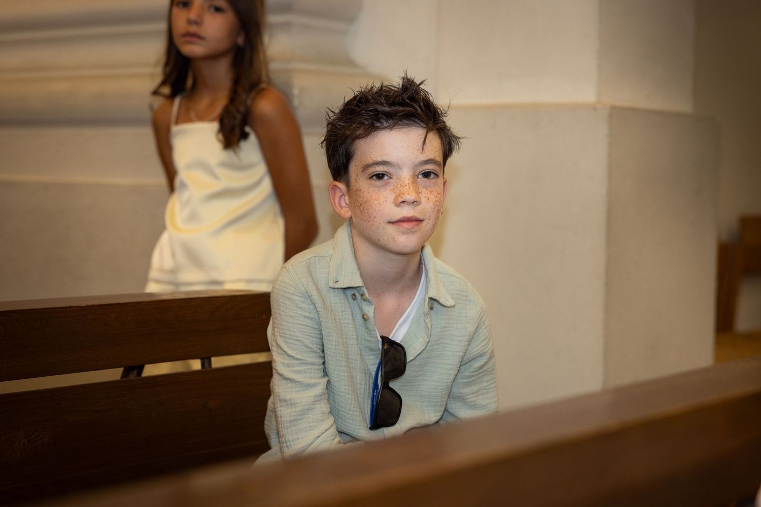 Ein Junge mit Sommersprossen und hellgrünem Hemd sitzt auf einer Kirchenbank und blickt ruhig in die Kamera.