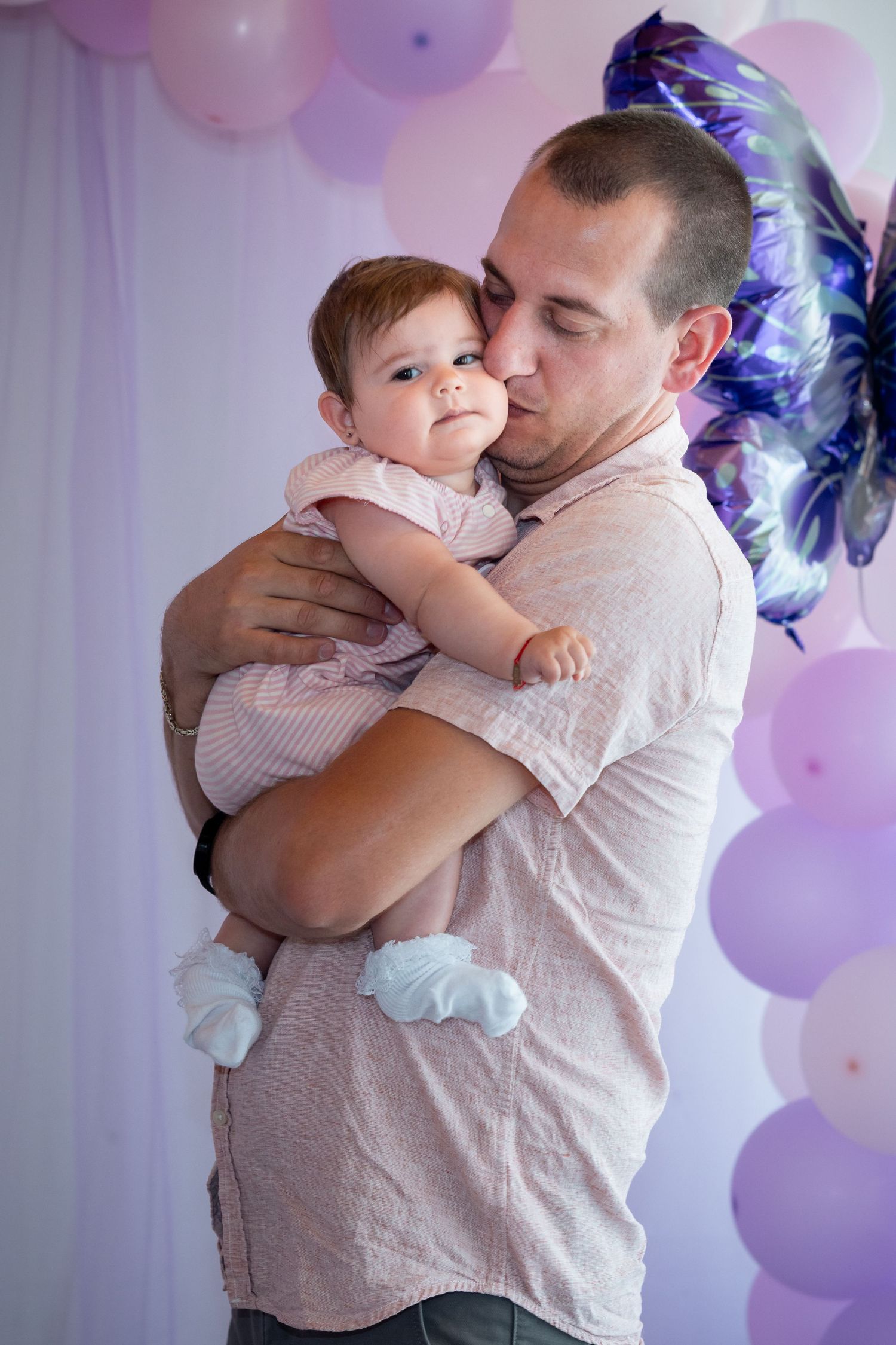 Ein Mann küsst Karoline auf die Wange vor rosa Ballons und einem großen Schmetterling.