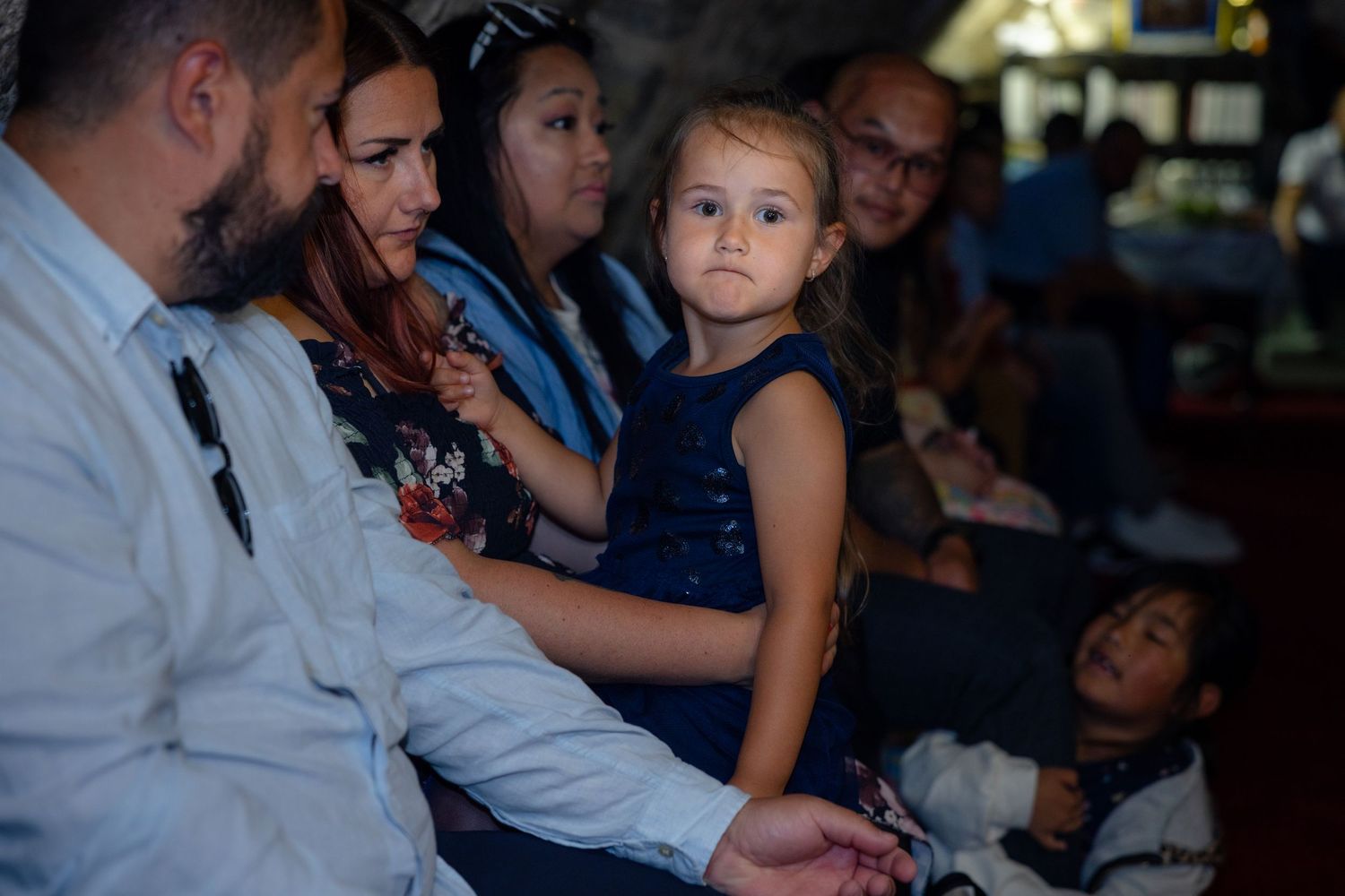 Ein junges Mädchen im dunkelblauen Kleid sitzt aufmerksam während der Familienfeier