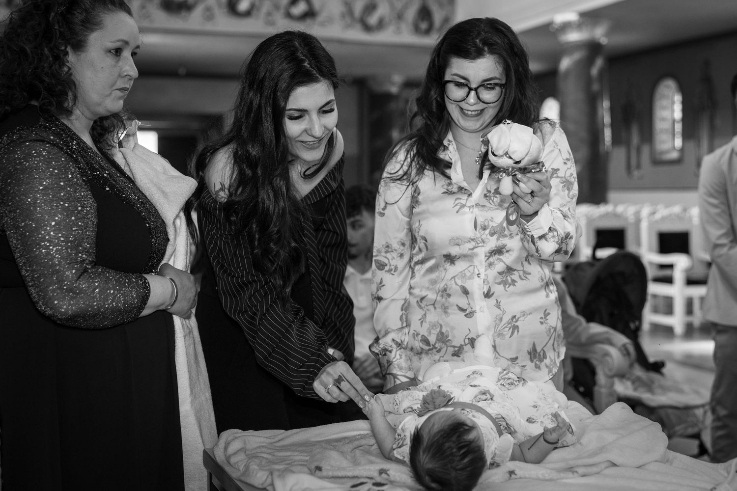 Women gathered around a newborn baby during a christening ceremony in a church, black and white photo.