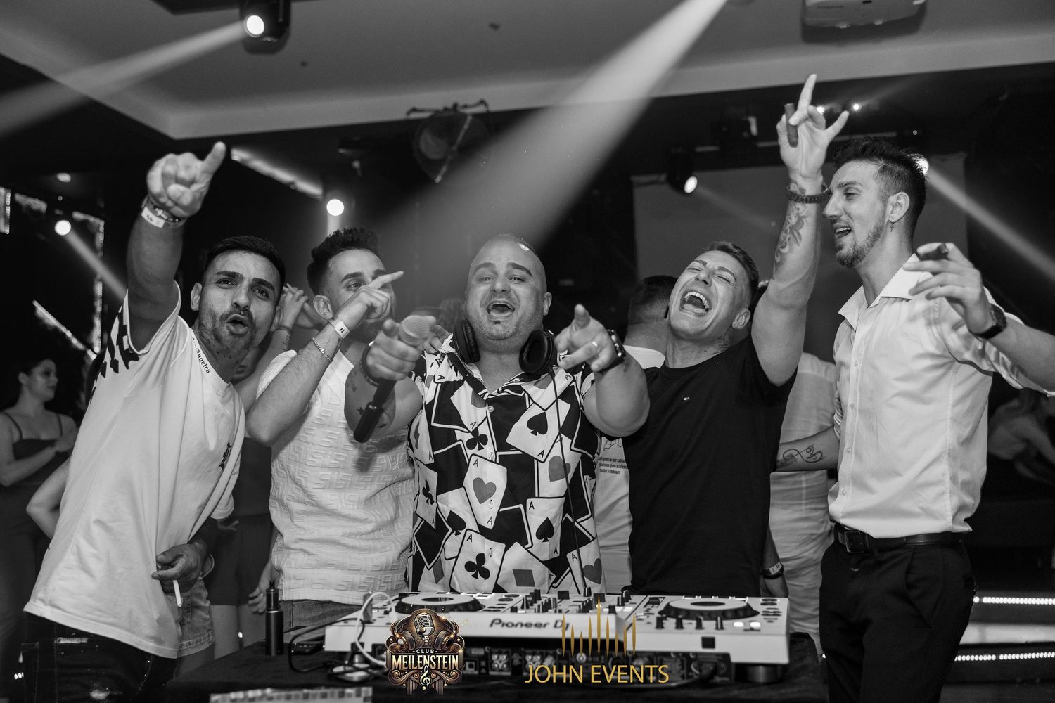 Schwarz-Weiß-Aufnahme einer Gruppe mit erhobenen Armen hinter dem DJ-Pult bei der Casino Party im Meilenstein.