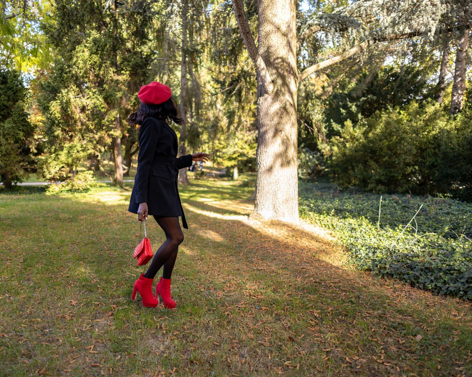 Jacky steht in Schwarz mit rotem Hut, Schuhen und Tasche auf einer Wiese im Park