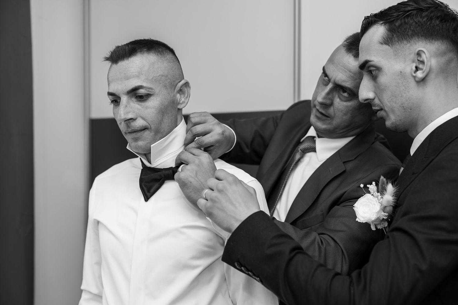 Two groomsmen help the groom adjust his bow tie and boutonniere before the wedding ceremony.