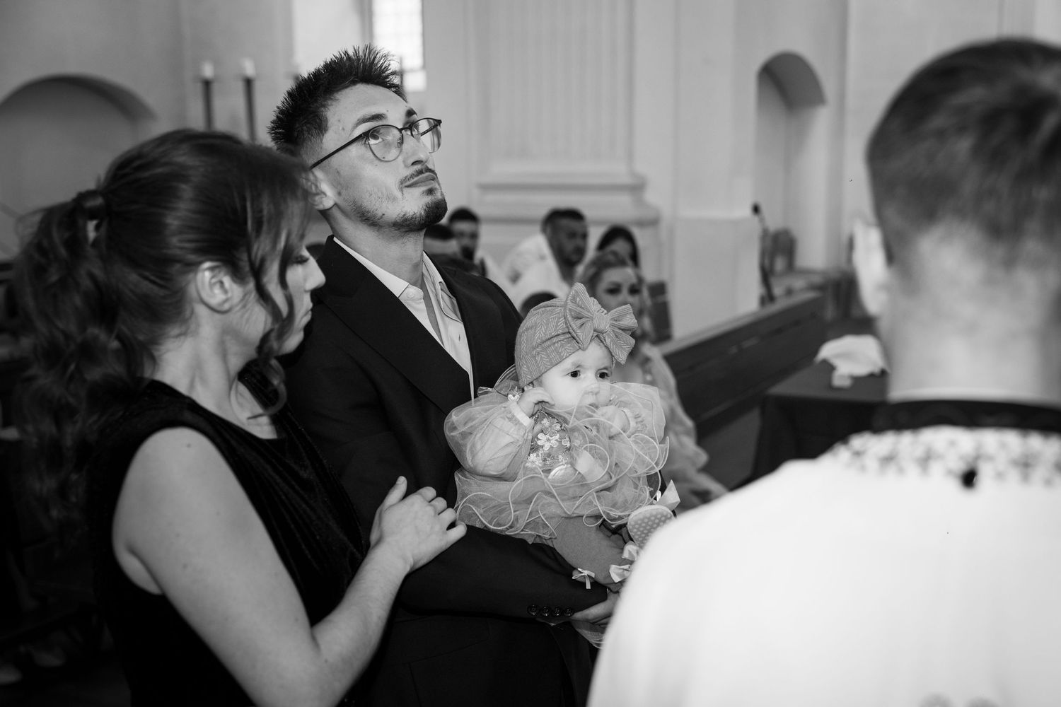 Black and white photo of a family with baby at a church ceremony, man in suit holding infant while seated in pew.
