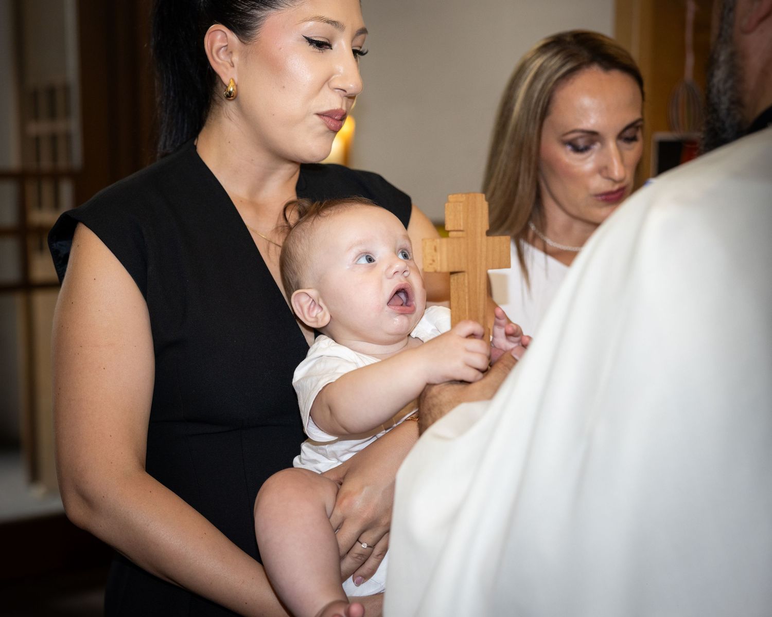 Aris greift auf dem Arm einer Frau nach dem Holzkreuz des Priesters.