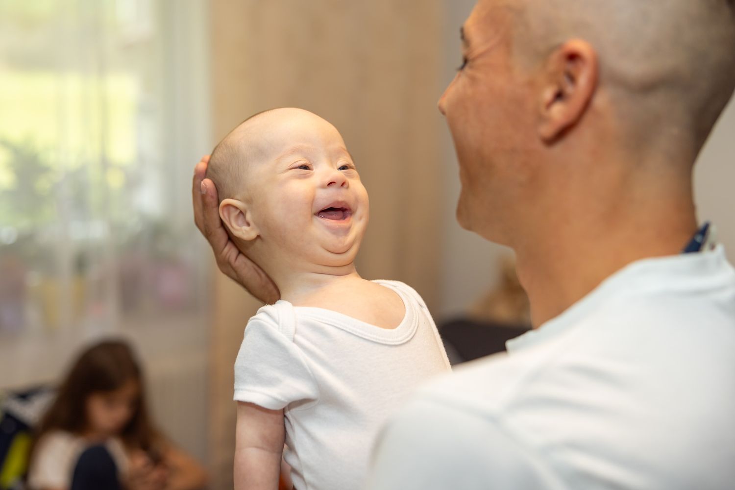 A bald baby laughing joyfully while being held by an adult, showing a happy bonding moment.