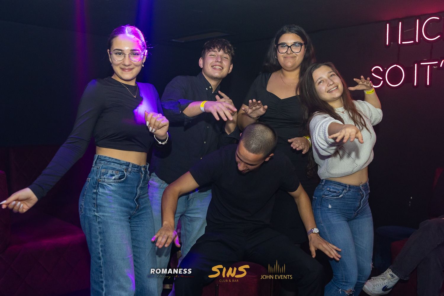 Eine kostümierte Gruppe posiert an Halloween im Club Sins vor einer Leuchtschrift.