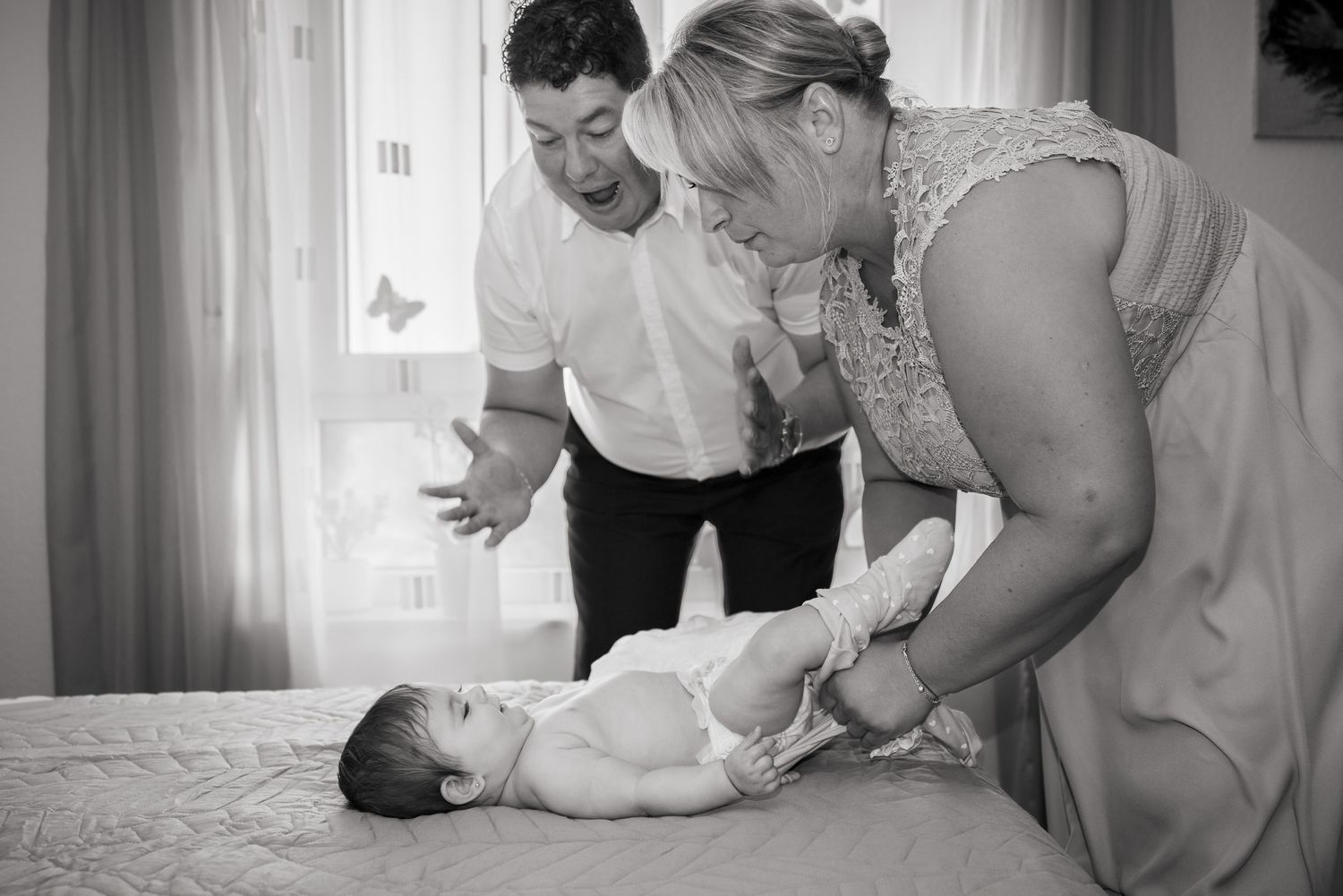 Schwarz-Weiß-Aufnahme eines Mannes und einer Frau, die Karoline auf dem Bett für ihre Taufe ankleiden.