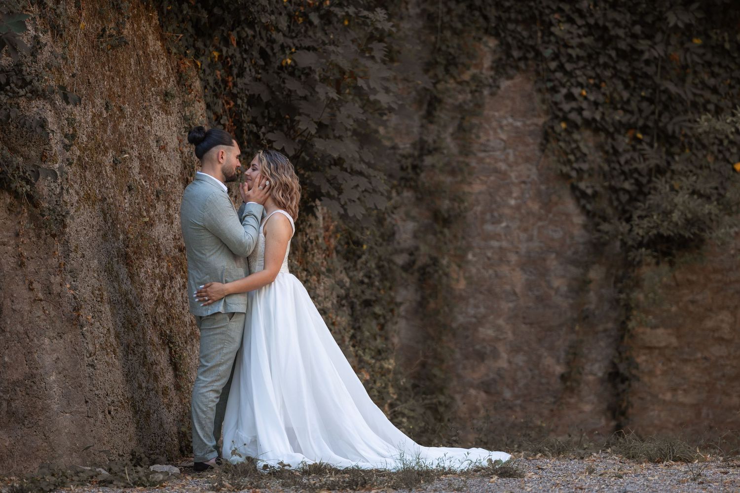 Bride and groom share a romantic kiss against a rustic stone wall outdoors on their wedding day.