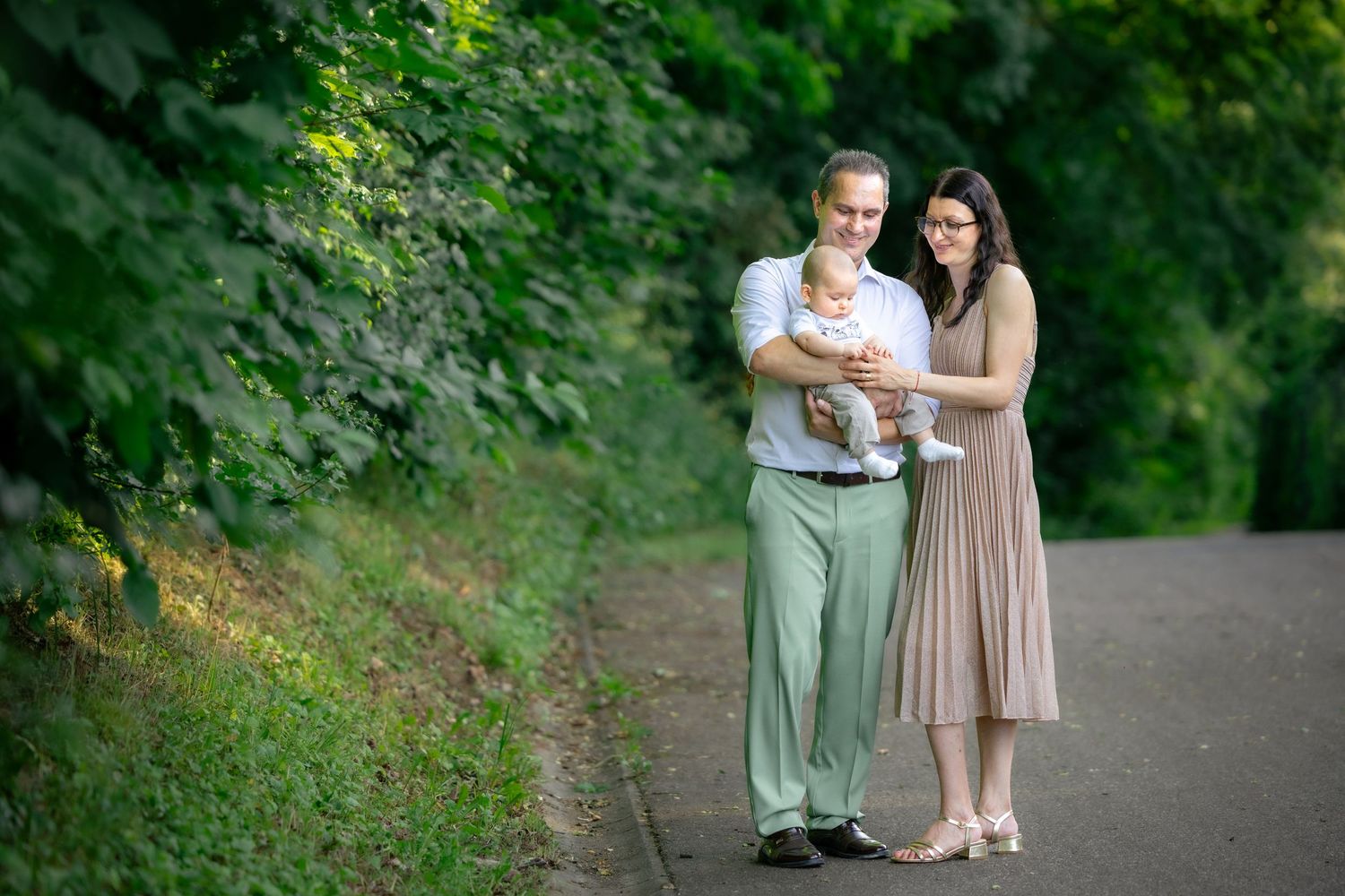 Zwei Erwachsene stehen mit Milan bei einem Familienporträt im Grünen.