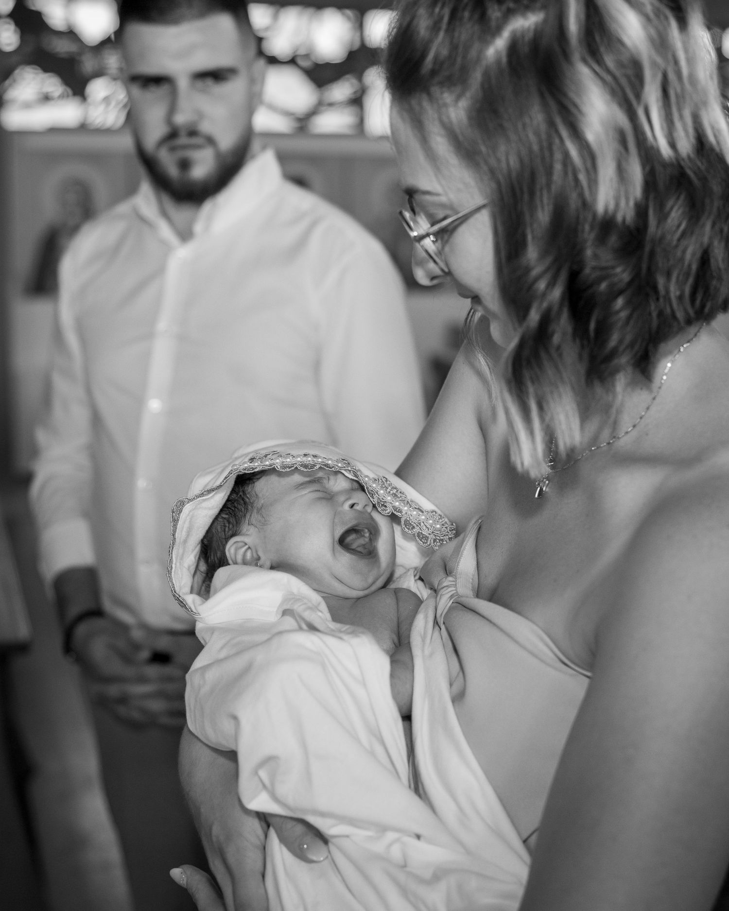 Emotional black and white photo of a newborn baby crying during a christening ceremony held by mother.