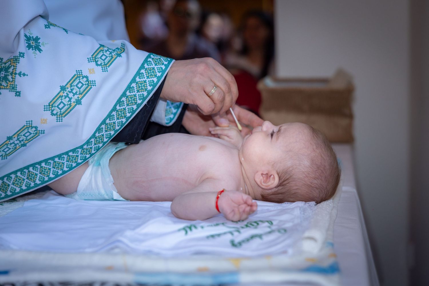 Priest performing a baptism ceremony on a newborn baby lying on a white cloth.