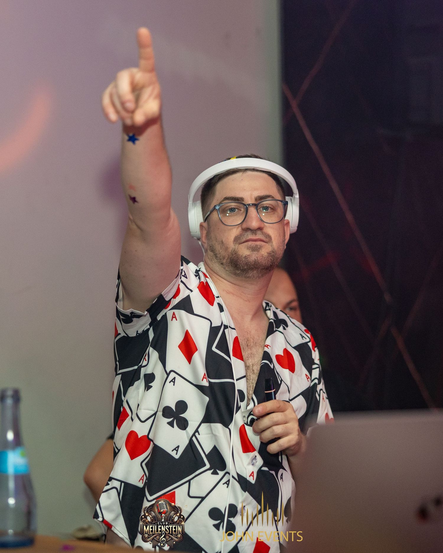 Ein Mann mit Brille hält ein Mikrofon und zeigt im Club Meilenstein nach oben.