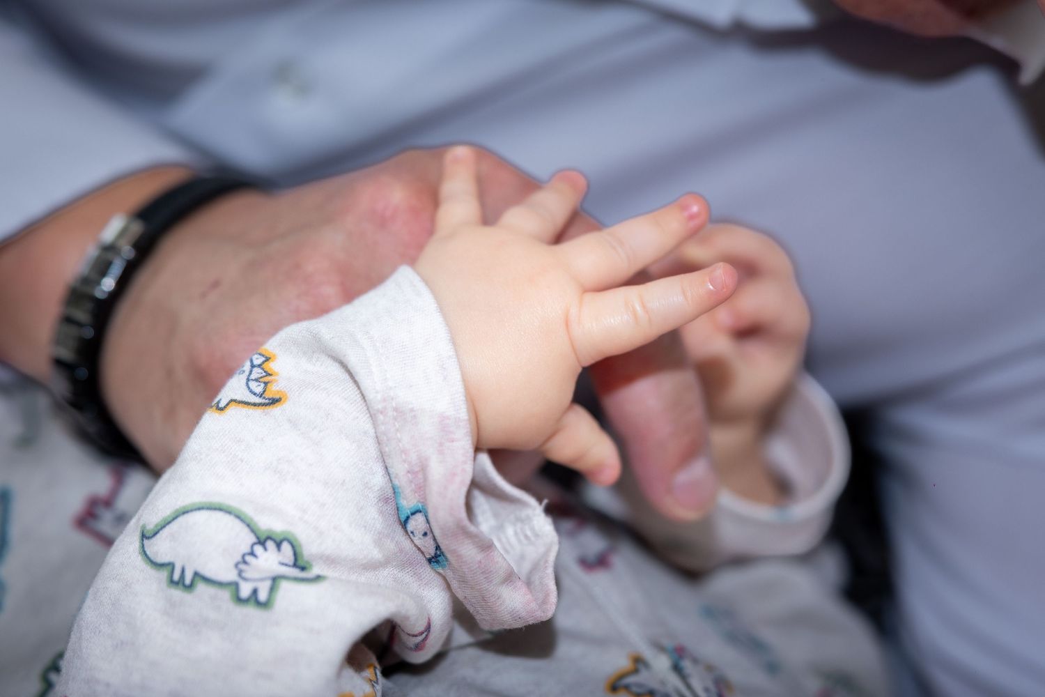 Nahaufnahme der kleinen Hände eines Babys, die die Hand seines Vaters umfassen.