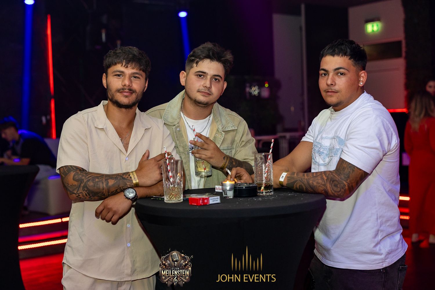 Drei Männer stehen an einem Tisch im Club Meilenstein zusammen.
