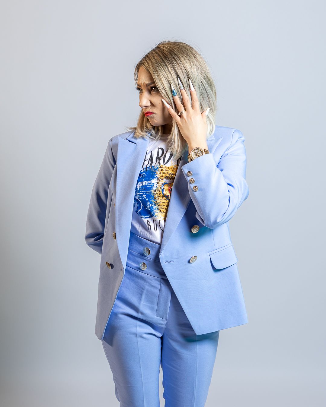 Woman in light blue blazer and matching pants poses confidently wearing a graphic tee and teal nail polish.