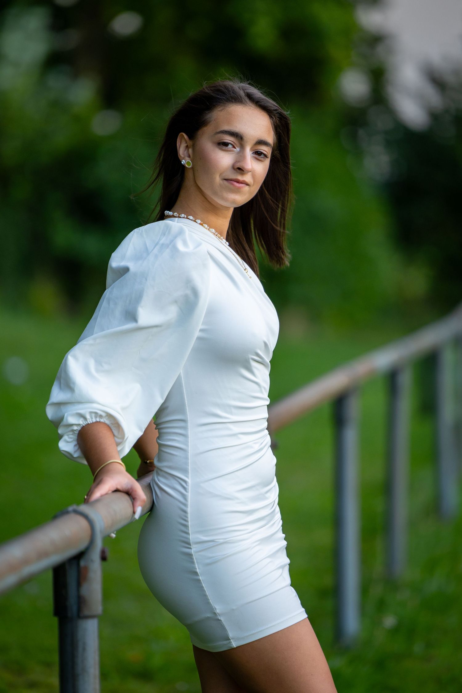 Eine junge Frau im weißen Kleid lehnt für ein Porträt an einem Geländer.