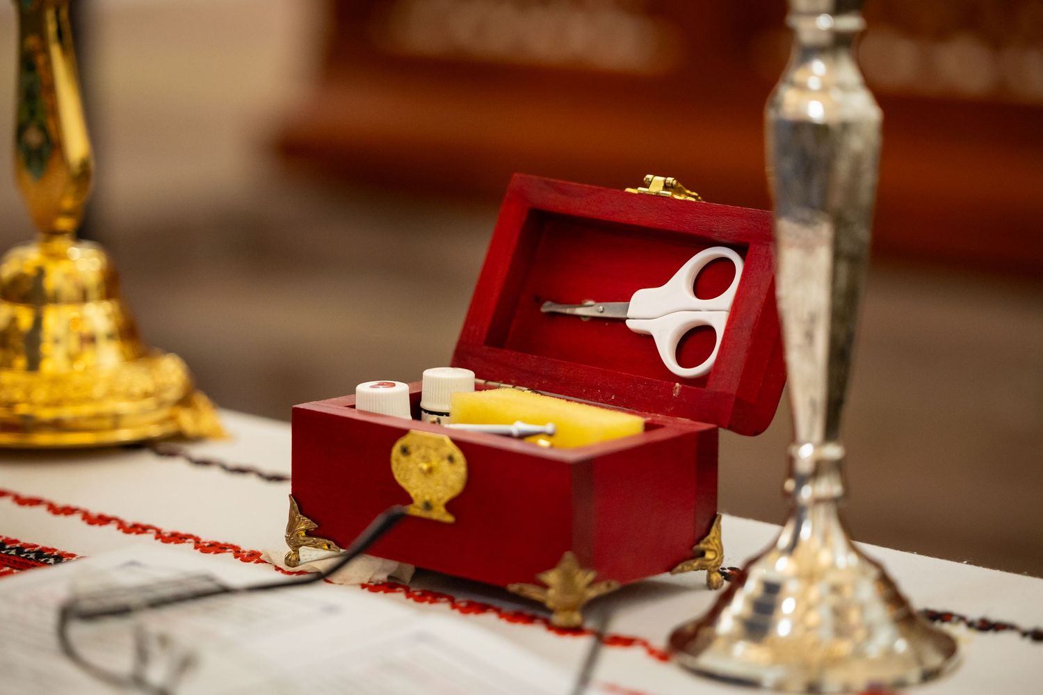Eine geöffnete rote Schatulle mit kleiner Schere, Fläschchen und gelbem Schwamm steht zwischen Kerzenständern.
