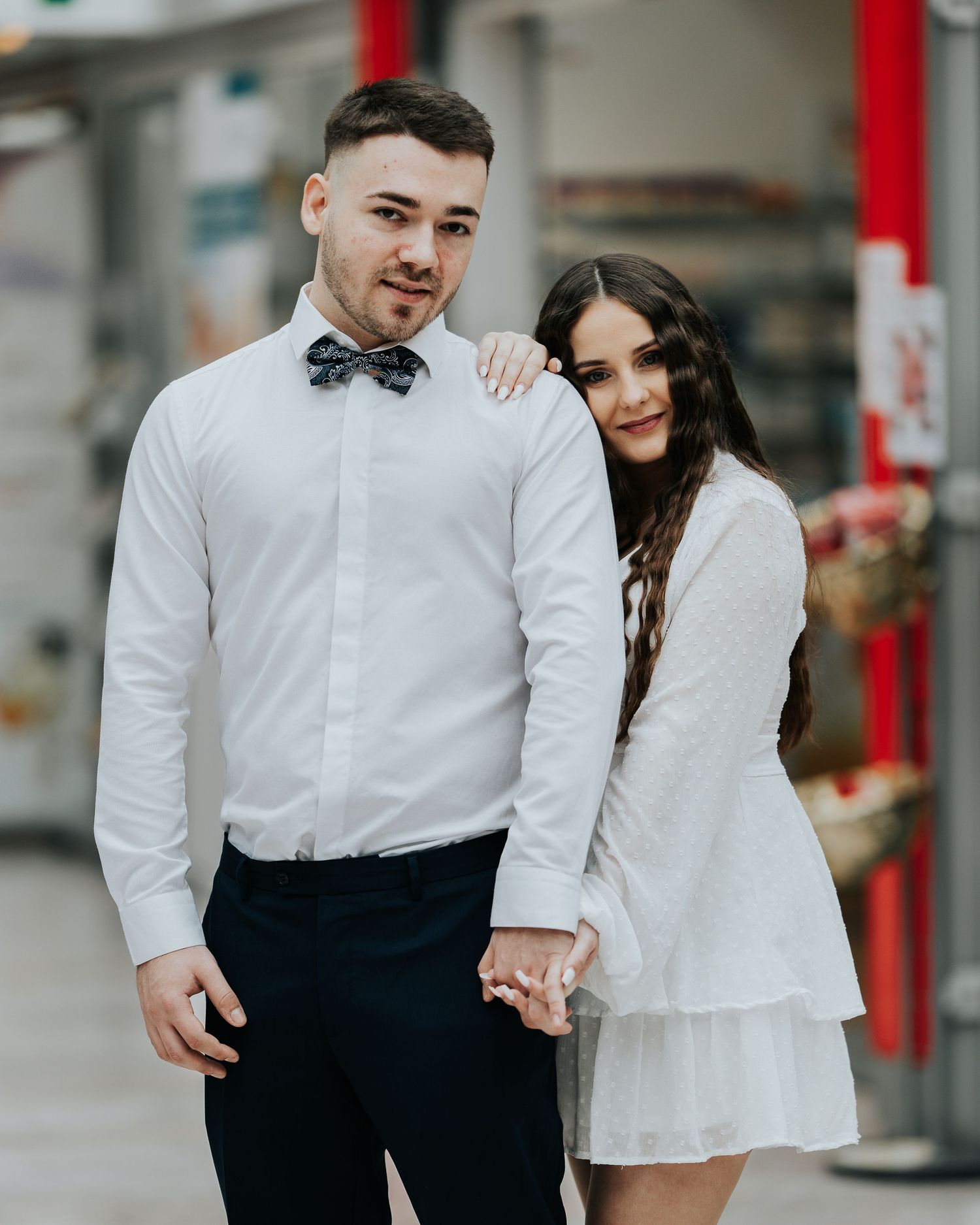 Madalin und Diana stehen Hand in Hand vor einem roten Element der Stadtkulisse.