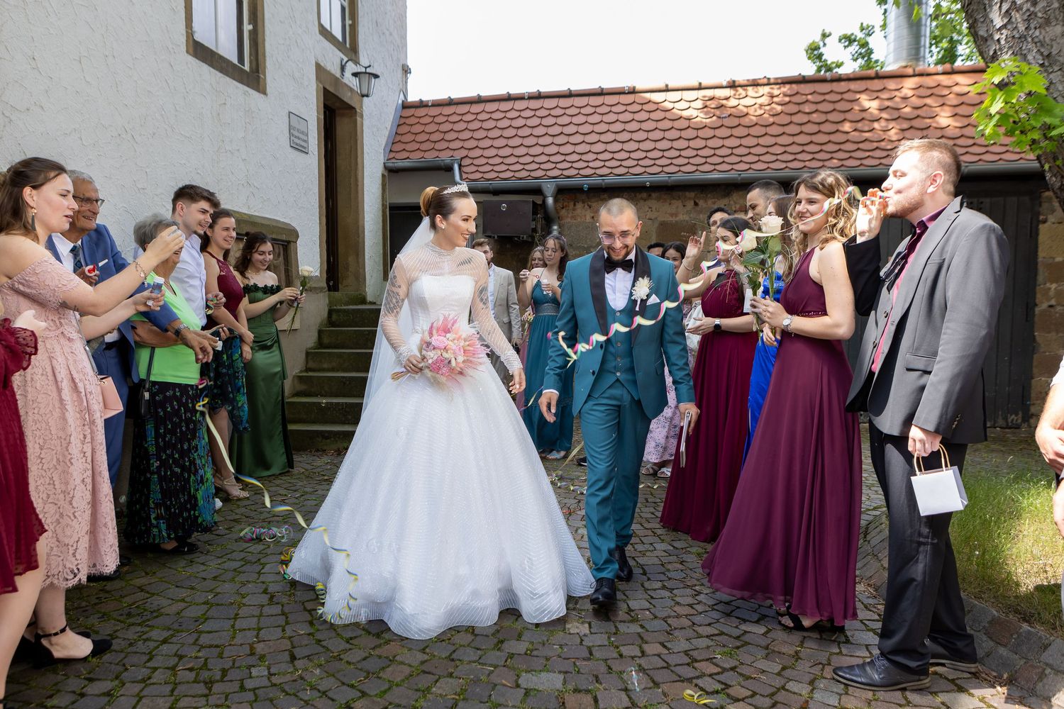 Brautpaar verlässt die Kirche zwischen Gästen und erhobenen Händen.