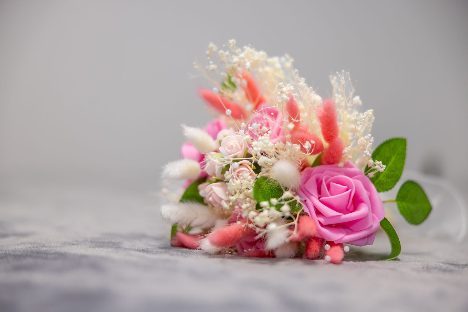 Pink and white floral bouquet with roses and wildflowers on a soft gray surface.