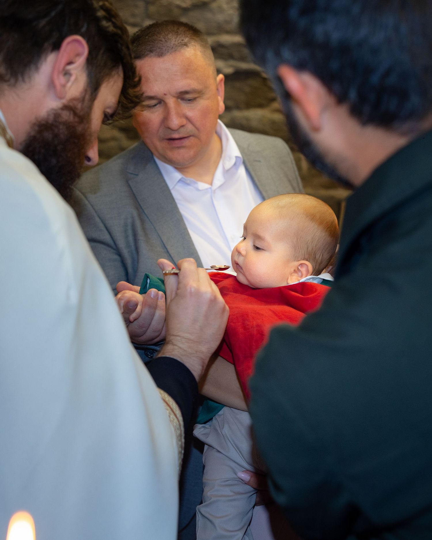 Milan wird in roter Kleidung gehalten, während der Priester vor ihm steht.