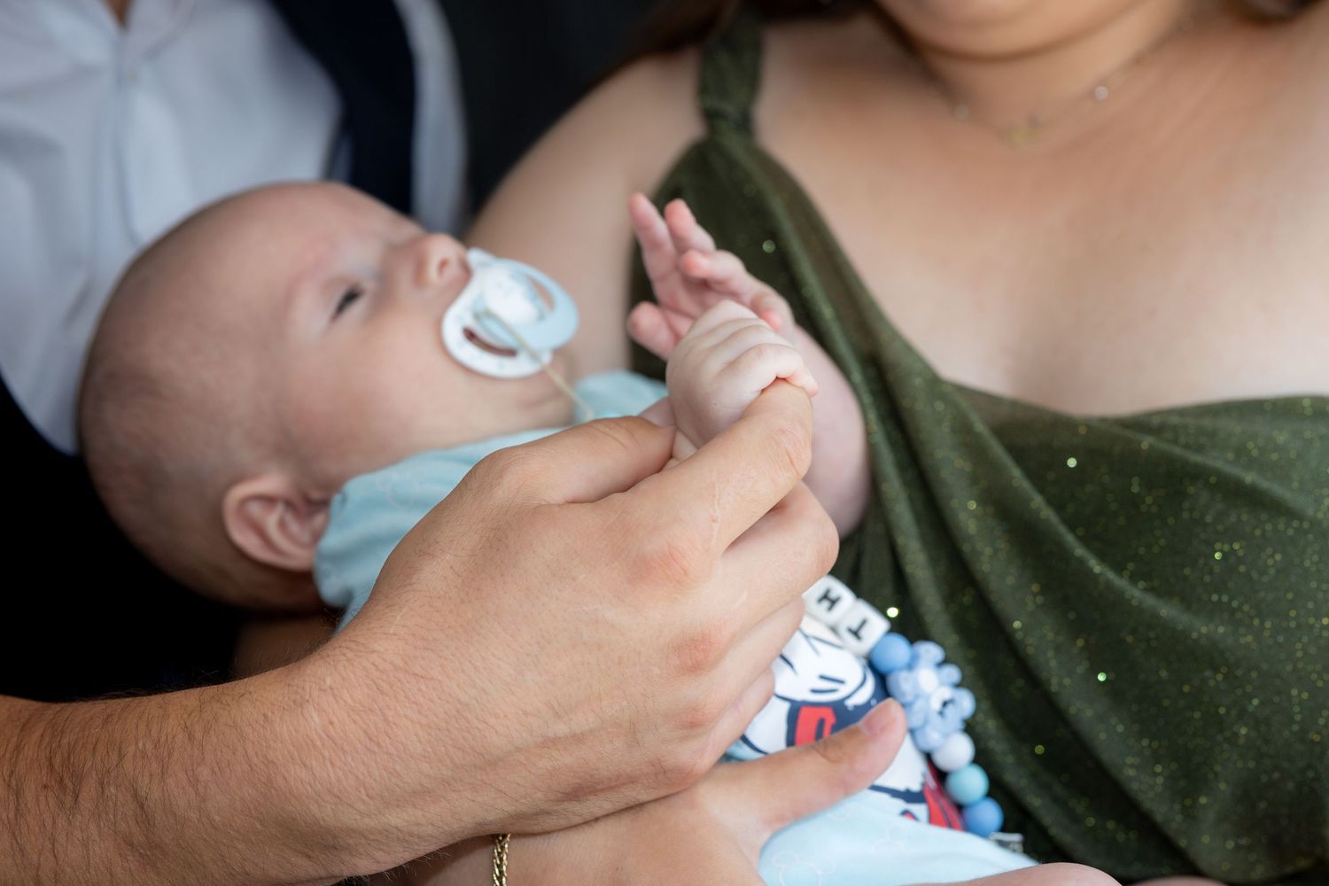 Eine erwachsene Hand berührt Theodors kleine Finger, während er mit Schnuller im Arm liegt.