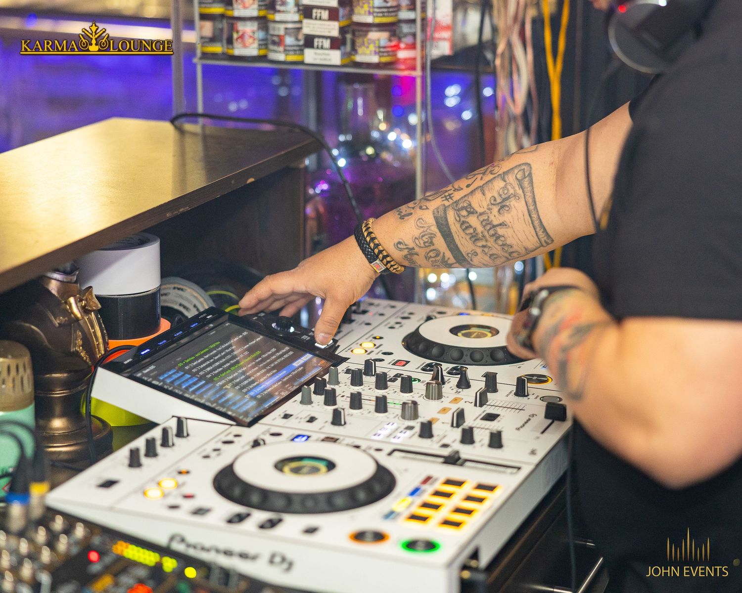 Hände bedienen das beleuchtete DJ-Mischpult in der Karma Lounge.