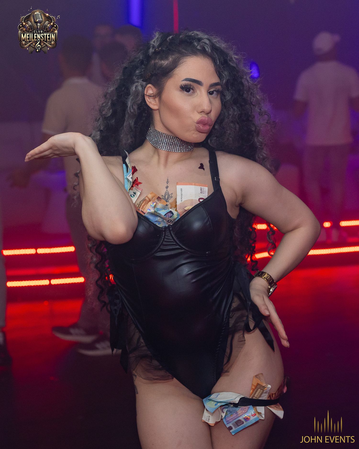 Eine Frau mit lockigen Haaren und schwarzem Bühnenkostüm vor roten Lichtstreifen im Club Meilenstein.