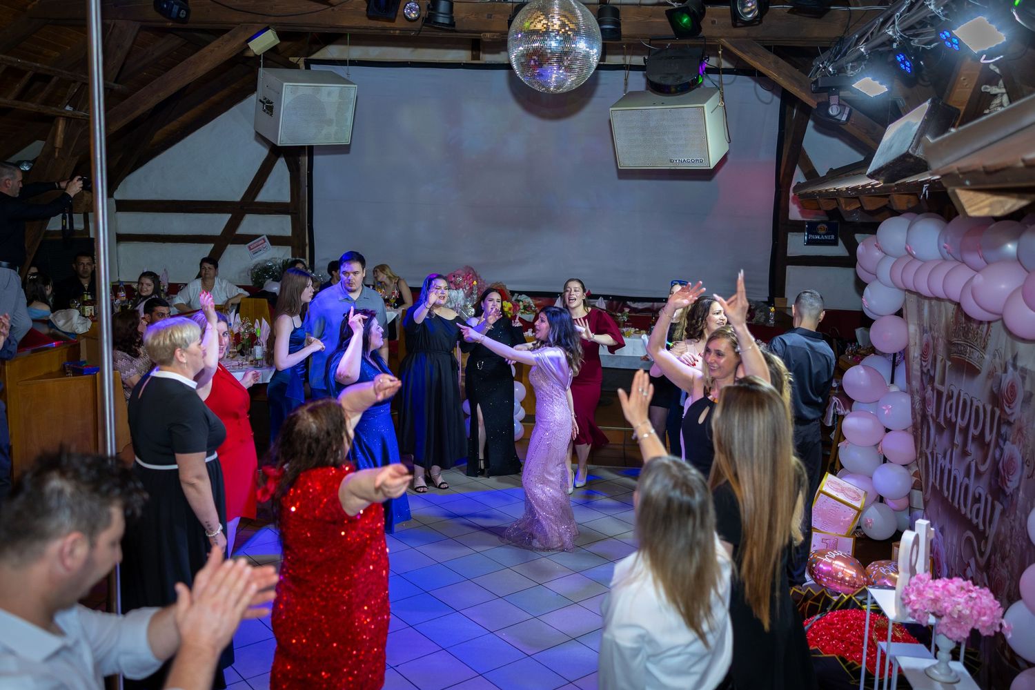 Gäste tanzen gemeinsam unter einer Discokugel und bunten Lichtern.
