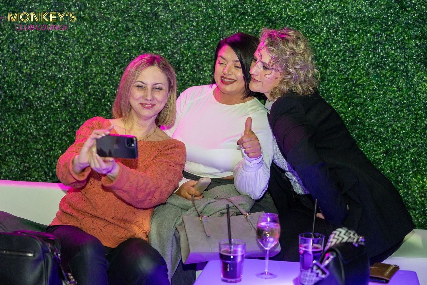 Drei Frauen machen auf einer Sitzbank im Monkey’s Club ein gemeinsames Selfie.