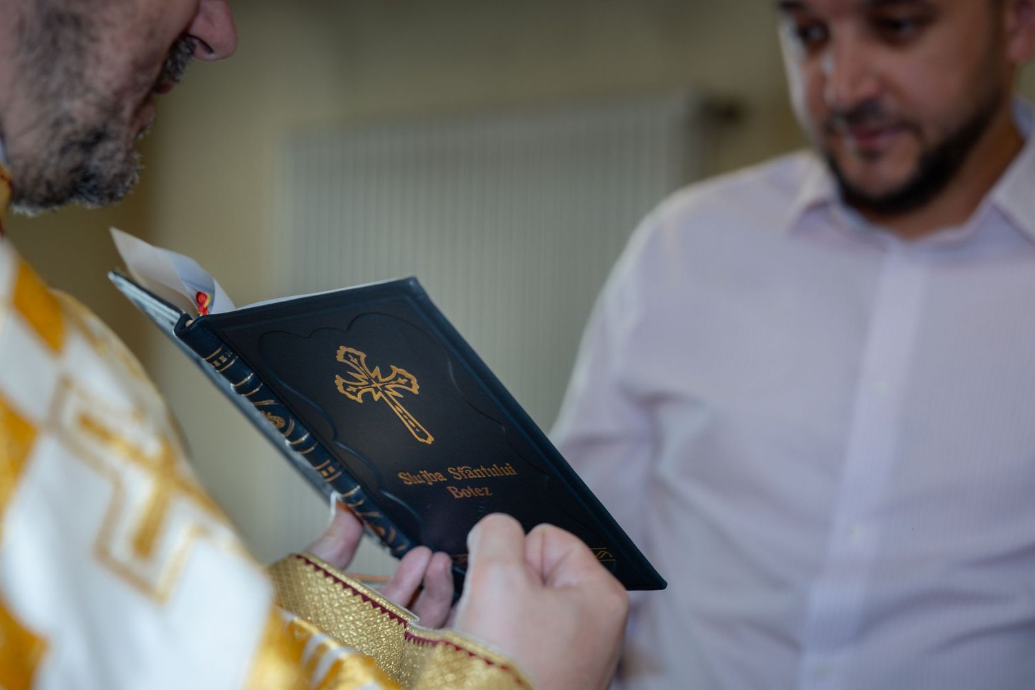 Das rumänische Buch zur Taufliturgie im Vordergrund, dahinter der Priester und ein Mann aus der Familie.