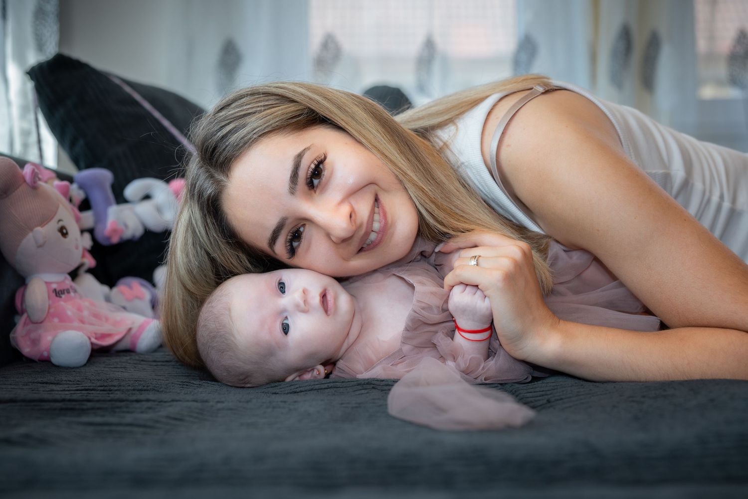 Eine lächelnde Frau liegt neben Lara auf dem Sofa und hält ihre kleine Hand.