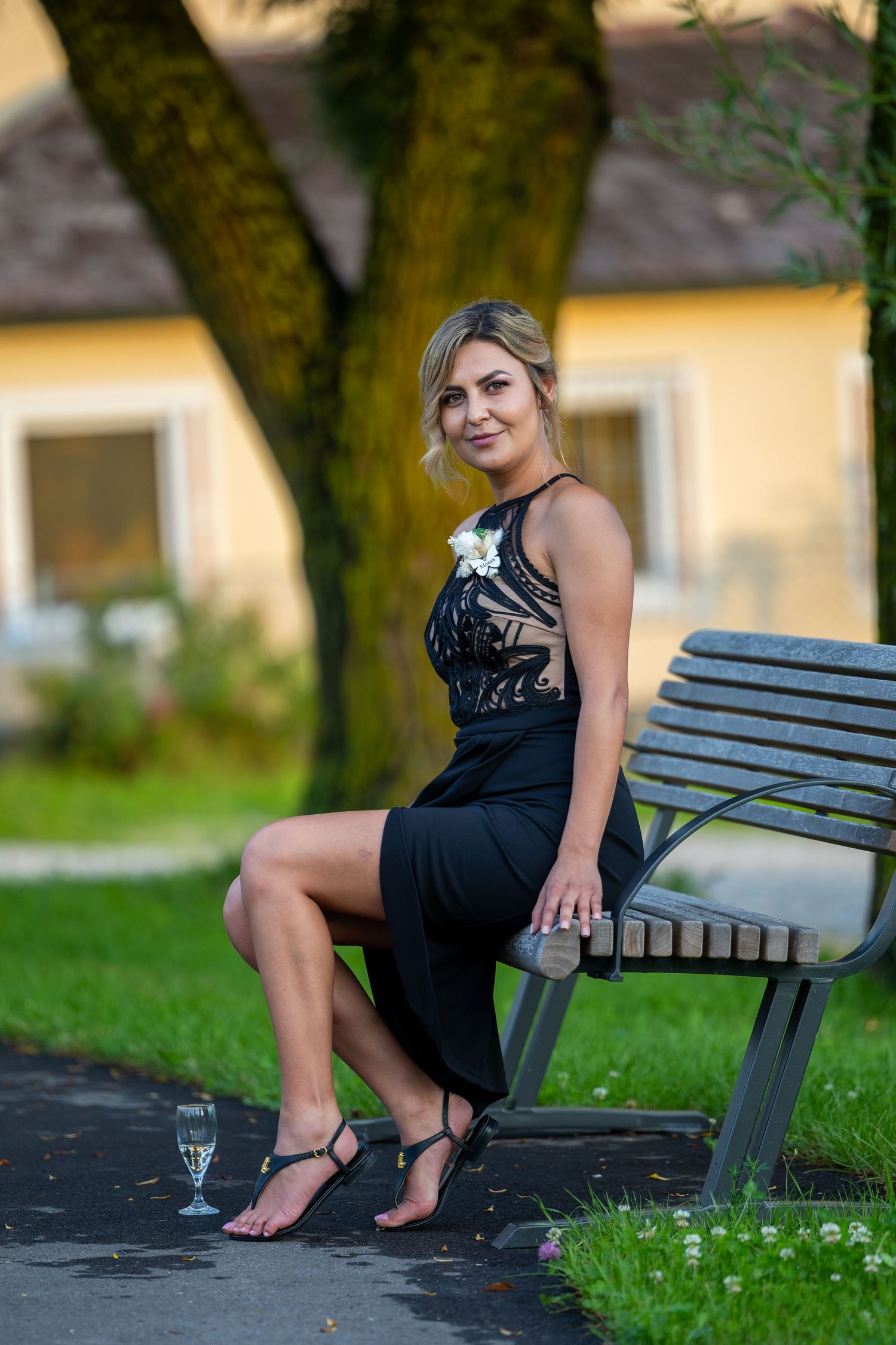 Eine Frau im schwarzen Kleid sitzt für ein Porträt auf einer Bank im Grünen.