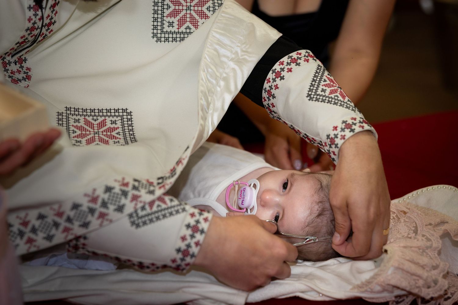 Der Priester berührt Alexia Ioanas Kopf, während sie mit einem Schnuller auf einem weißen Kissen liegt.