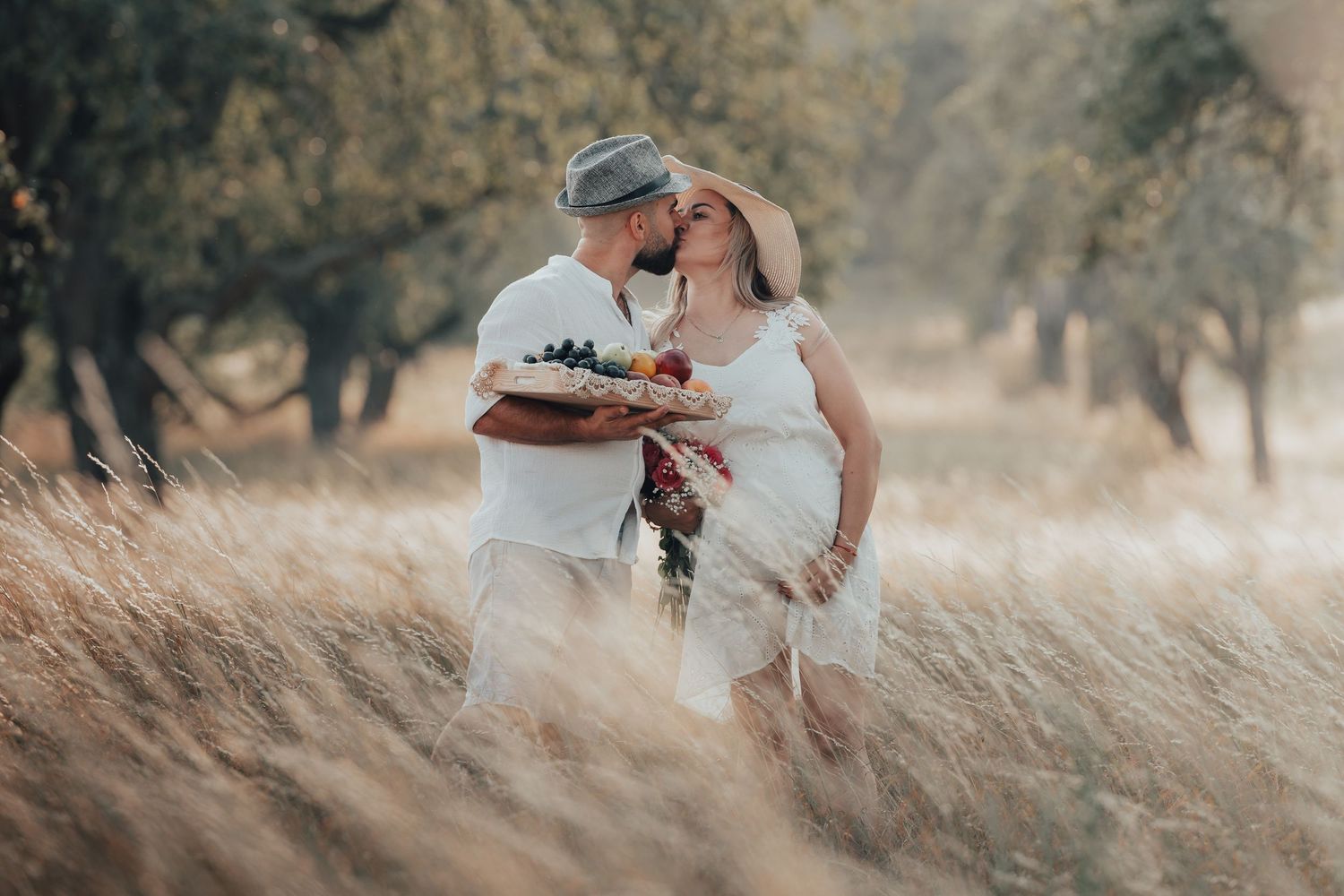 Romantic couple kissing in a golden wheat field, woman in white dress holding a colorful bouquet.