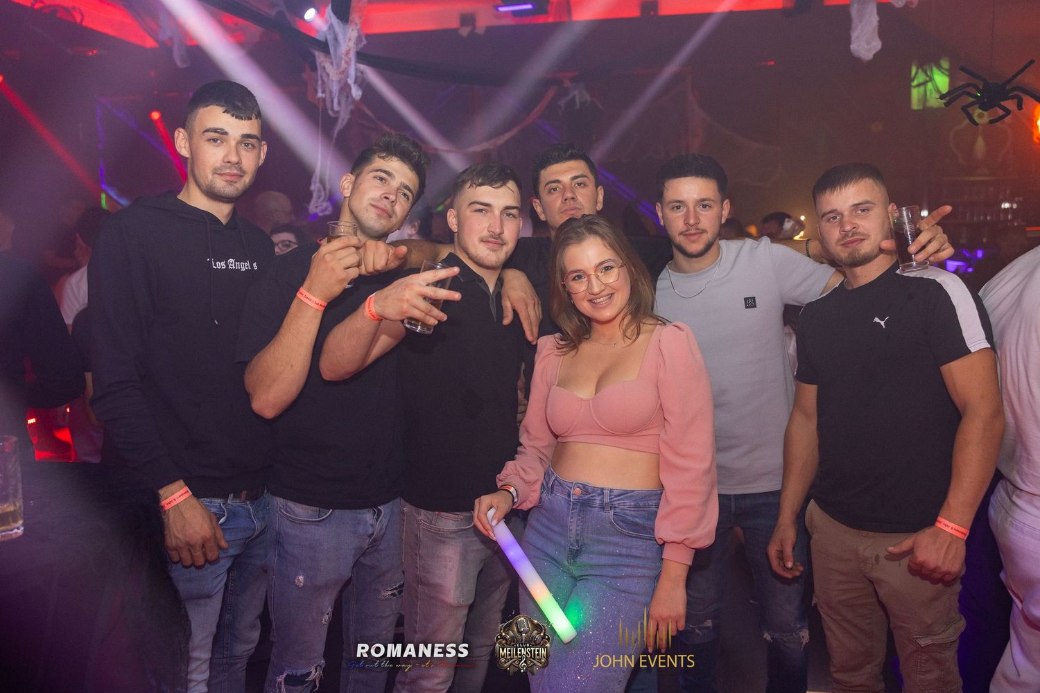 Eine Gruppe steht an Halloween unter farbigem Licht im Club Meilenstein zusammen.