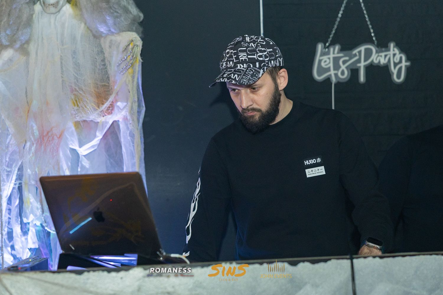 Ein DJ mit schwarzer Kappe arbeitet am Pult neben der Halloweendekoration im Club Sins.