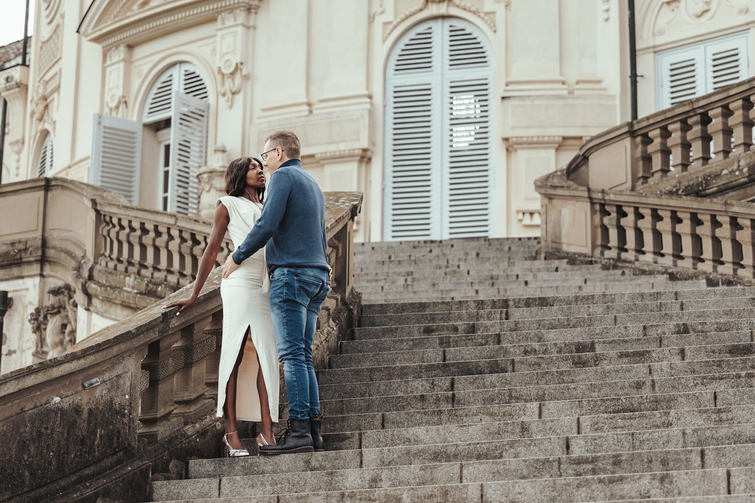 Romantic couple embracing on grand stone steps of a classical European building.