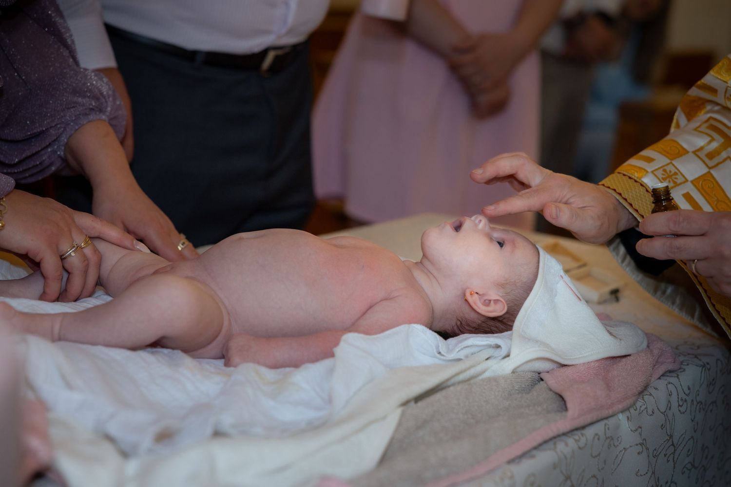 Lara Ștefania liegt auf einem weißen Tuch, während der Priester bei der Taufe ihre Stirn berührt.