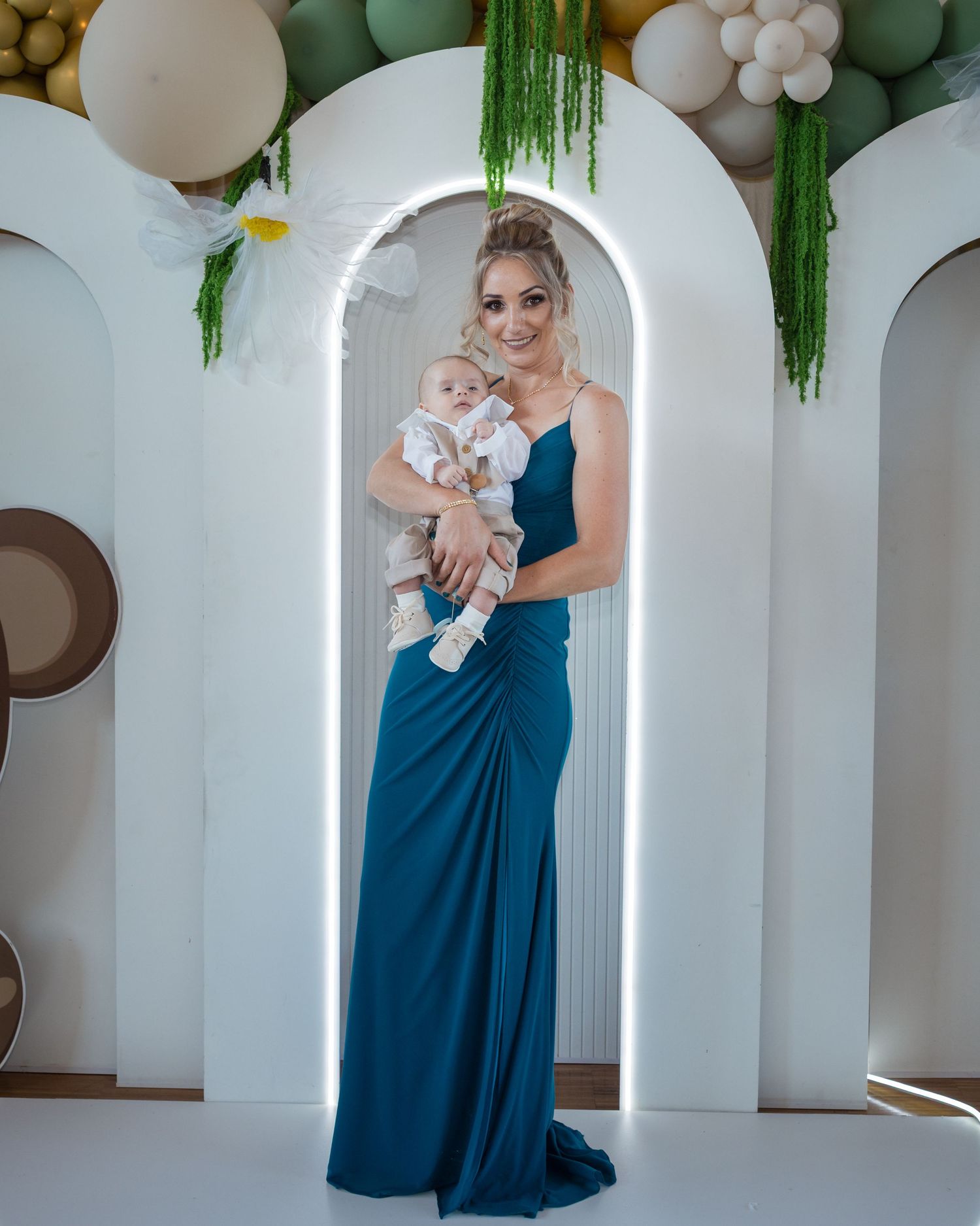 Eine Frau im langen blauen Kleid trägt Theodor vor einer weißen Kulisse mit Luftballons.
