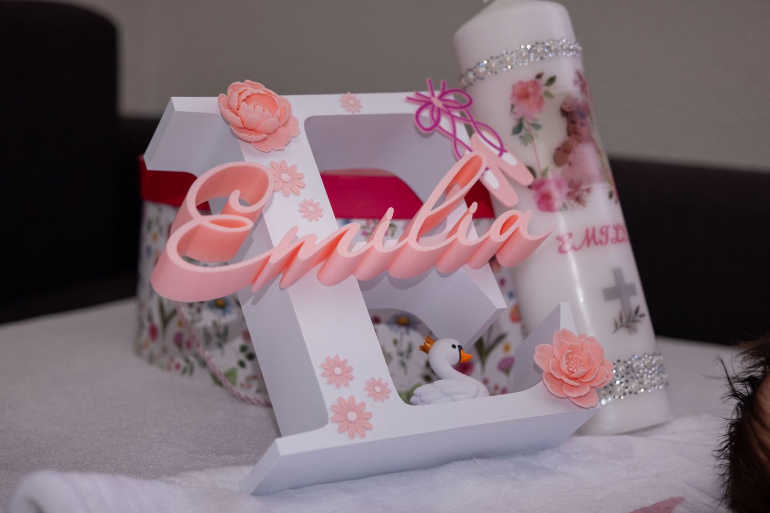 Ein dekorativer Namensrahmen und eine Taufkerze für Emilia auf einem Tisch.