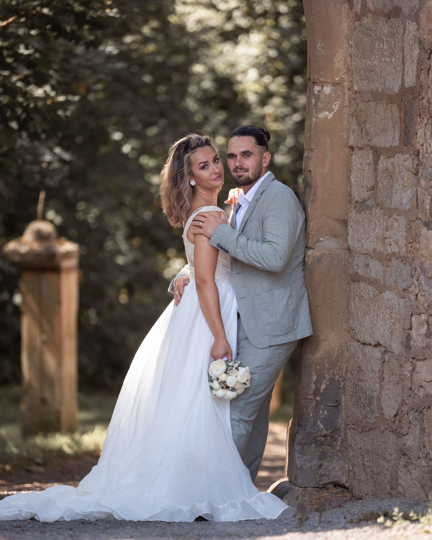 Naomi und Sergiu stehen gemeinsam neben einem alten Steinpfeiler.