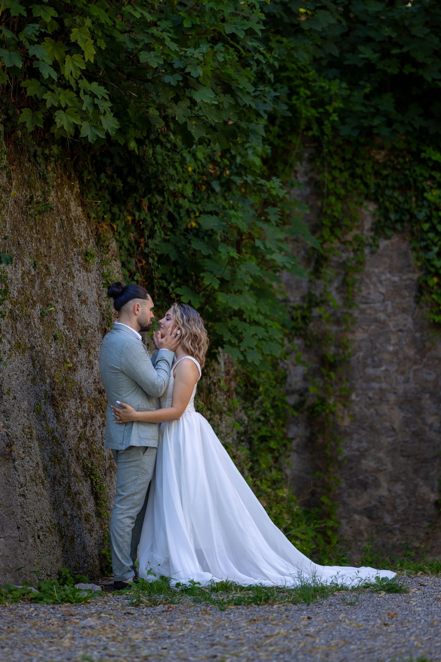 Naomi und Sergiu stehen eng beieinander vor einer von Efeu bewachsenen Steinmauer.