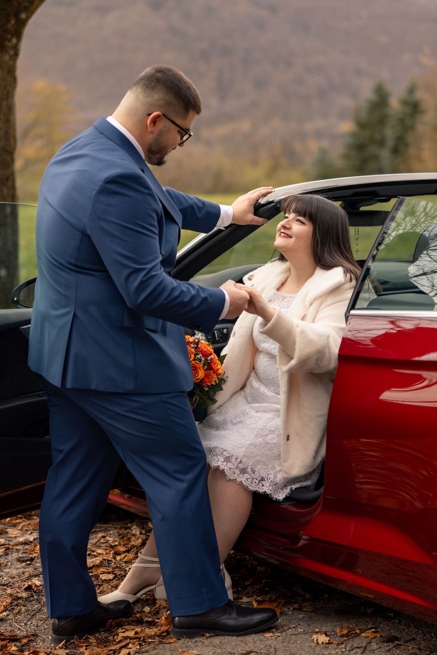 Leon hilft Diana beim Aussteigen aus dem roten Auto vor dem Paarshooting