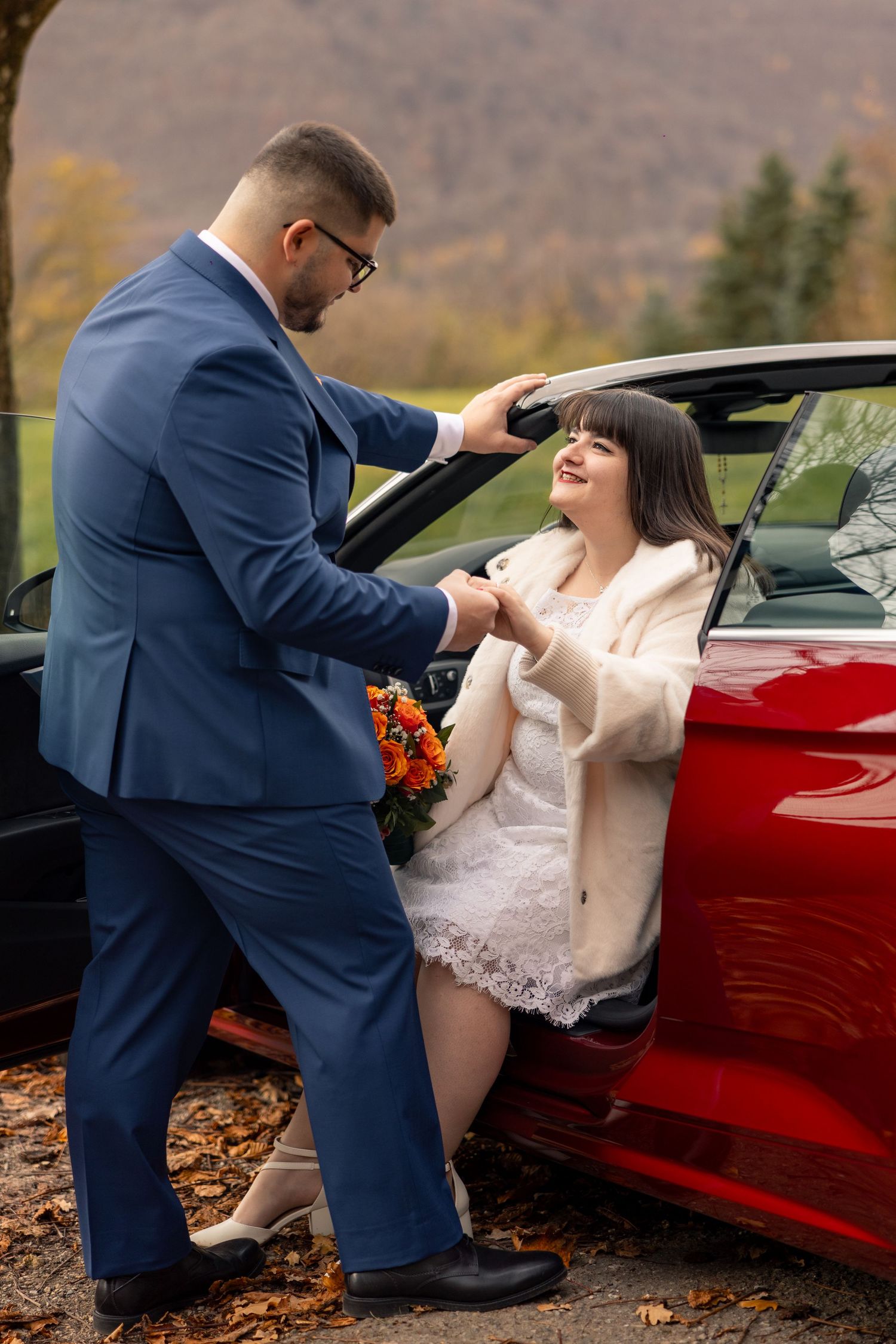 Bräutigam hilft der Braut aus dem roten Auto