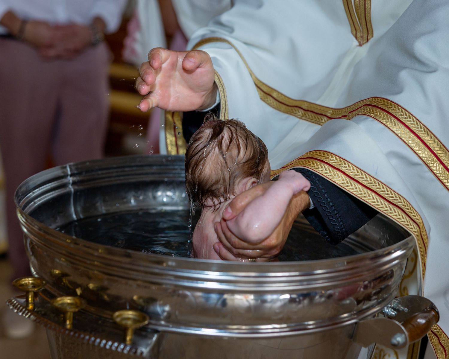 Ein Baby wird während des Taufrituals über einem metallenen Becken gehalten.