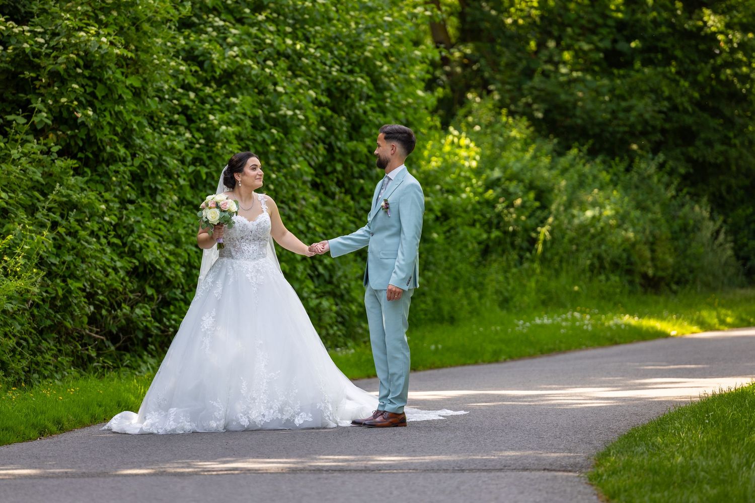 Angeliki und Dominik gehen Hand in Hand über einen Weg zwischen grünen Bäumen.