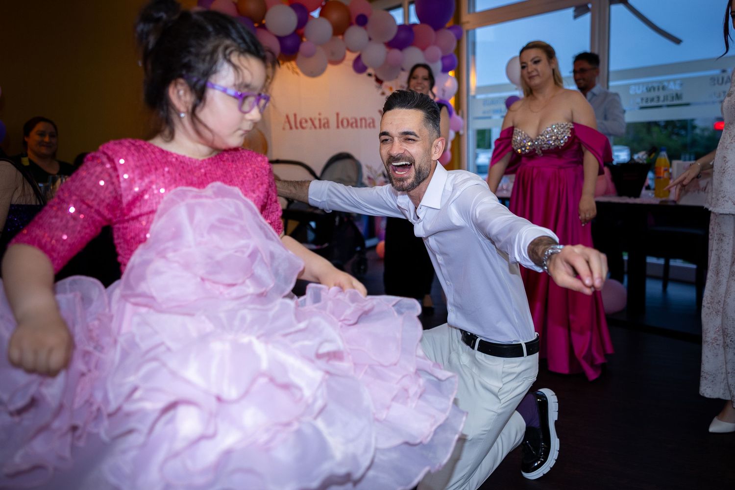 Ein lachender Vater tanzt mit einem Mädchen im rosa Festkleid bei der Feier zur Taufe seiner Tochter.