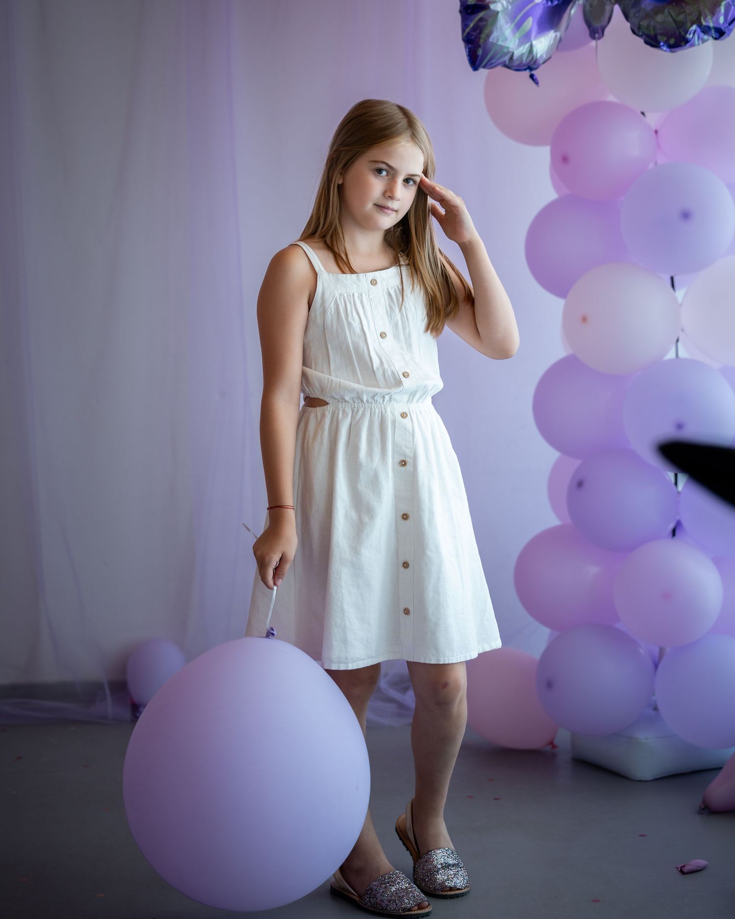 Ein Mädchen im weißen Kleid steht mit einem großen Luftballon neben der rosa Ballondekoration.